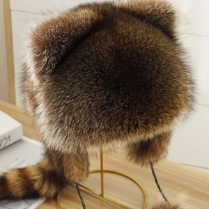 Faux fur raccoon tail hat with ear flaps and tail pendant on metal display stand