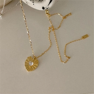 Detailed view of gold heart pendant necklace with sunburst texture and center zircon stone