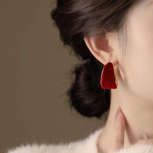 Close-up of elegant red velvet heart-shaped earrings with gold trim worn by a model