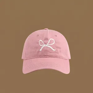 Close-up of pink cotton baseball cap with white embroidered bow and curved brim
