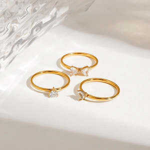 Three gold stainless steel rings set with heart-shaped crystals on wave glass background