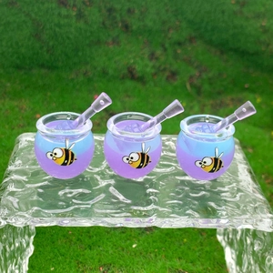 Three gradient purple honey jars with bee patterns and stirrers on glass over grass