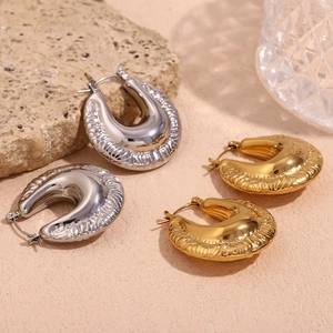 Detail of chunky gold and silver U-shape hoop earrings with textured stripes on stone