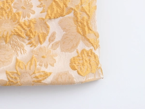 Nahaufnahme von beigem Jacquard-Stoff mit detaillierter 3D-Goldblumenstickerei