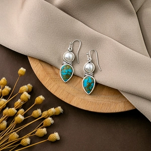 Detail view of bohemian drop earrings with turquoise stones and white pearls on wood