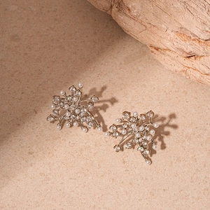 Detail shot of silver flower earrings with white pearls and zircons on sandy stone background