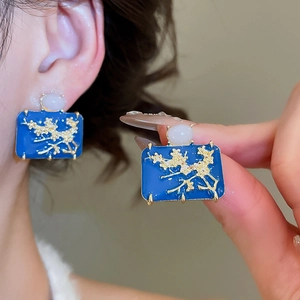 Detailed view of blue enamel plum blossom earrings with gold floral relief and white bead