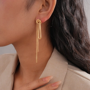 Close-up of elegant gold tassel knot earrings on model in professional business attire