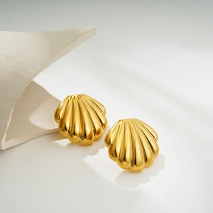 Close-up of gold shell stud earrings on white stone background with soft shadows