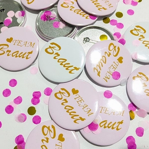 Detailed close-up of pink and white TEAM Braut tinplate badges for wedding parties