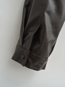 Detailed close-up of dark brown faux leather jacket cuff with stitching and button