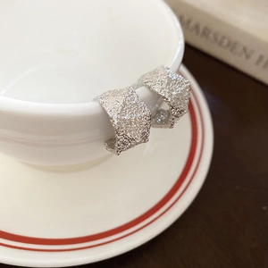 Detail shot of silver textured C-shape earrings hanging on a white ceramic coffee cup rim