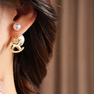Close-up of a pearl stud earring with a hanging golden rocking horse charm on the ear
