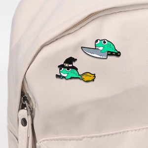 Cartoon green enamel frog pins set with witch and dagger designs on beige backpack
