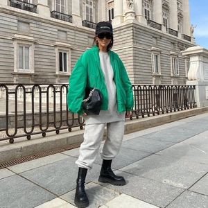 Street style shot of a vibrant green bomber jacket paired with a grey hoodie and black boots