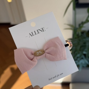 Detail of pink cotton bow hair tie with oval charm and clear amber bead on branded card