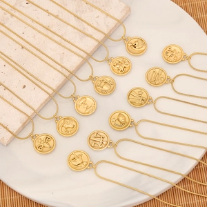Set aus 12 goldenen Edelstahl-Halsketten mit Sternzeichen auf Marmorplatte präsentiert