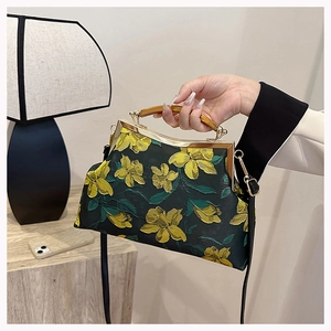Detail of black embroidered floral handbag with wooden handle and gold frame