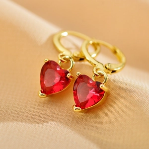 Macro shot of gold hoop earrings with red heart-shaped gemstone pendants on soft fabric