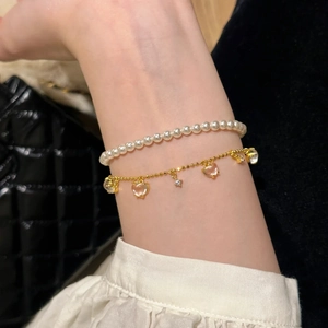 Detail of layered gold heart charm bracelet and pearl strand on model wrist