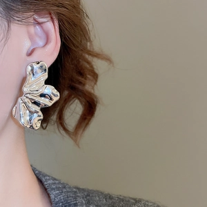Close-up of a silver irregular wave textured metallic earring worn on a model's ear