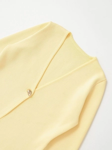 Gros plan d'un gilet en maille jaune pâle avec col en V et bouton doré asymétrique