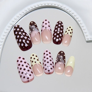 Uñas postizas de lunares en tonos chocolate y rosa presentadas sobre un espejo redondo