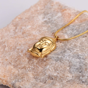 Polished golden Buddha head pendant necklace with snake chain on natural stone background
