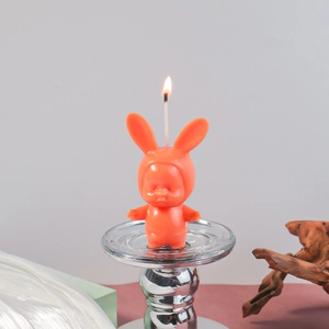 Close-up of a lit orange bunny baby candle on a glass stand with warm background