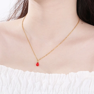 Dettaglio di una collana a catena dorata con pendente fragola rosso acceso su un modello