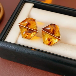 Macro view of amber resin geometric earrings with gold trim in a premium black jewelry box