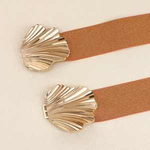 Detail eines orangen elastischen Gürtels mit goldenen Muschelschnallen auf Stoff