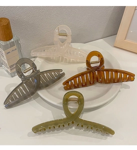 Detail of four large acetate hair claws in pastel tones on a white ceramic plate