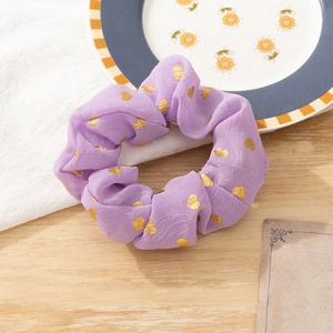 Detail view of purple chiffon hair scrunchie with gold heart pattern on wooden surface