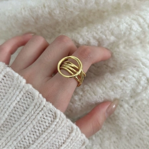 Detail of layered gold ring with circular cutout worn over white knit sweater