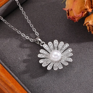 Gros plan du pendentif marguerite avec perle et cristaux sur un plateau texturé gris