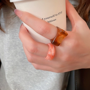 Close-up of amber brown and marble pink resin rings worn while holding a coffee cup