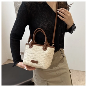 Detail view of woven straw tote bag featuring leather handles and knotted strap accents