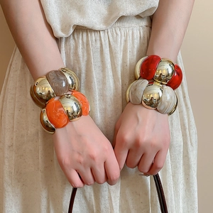 Chunky geometric acrylic and gold metal bracelets on wrist with pleated styling