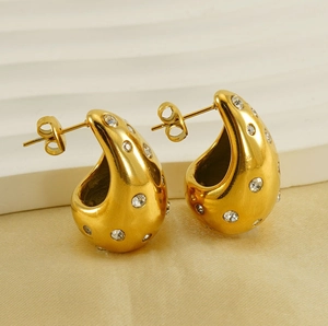 Macro shot of chunky gold teardrop earrings with embedded crystals on textured fabric