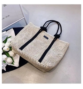 Close-up of beige woven tote bag featuring black cotton rope handles and decorative straps