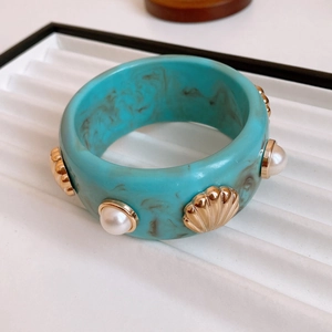 Close-up of gold-plated bangle featuring turquoise resin, shells and white pearls