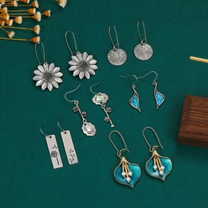 Detailed flat lay of bohemian earrings with sunflower, leaf, and enamel pearl designs