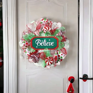Detail of a red, white and green Christmas wreath with a Believe sign on a white door