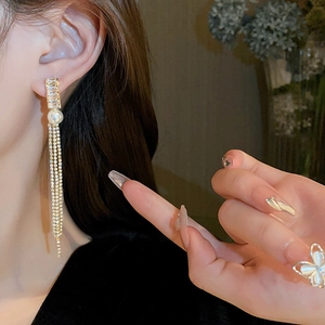 Close-up of elegant gold tassel earrings with white pearls and sparkling rhinestones on model