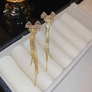 Detailed macro shot of elegant gold bow earrings with crystal tassels in a white jewelry box