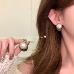 Macro shot of retro leopard print and white pearl pendant earrings worn on the ear