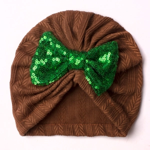 Detailed view of brown knitted baby turban hat with a large green sequin bow decoration