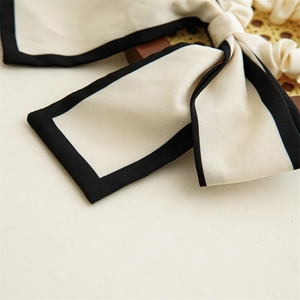 Detail of a French style beige hair scrunchie with black trim and long ribbon streamers