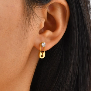 Close-up of gold safety pin earrings with a round zircon stone on the model's ear